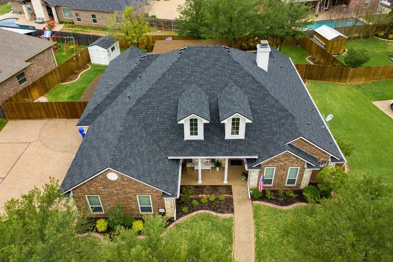 Aerial view of a brick home with a completed shingle roof